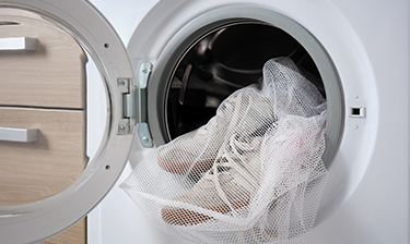 White shoes in a mesh laundry bag being inserted into the washing machine.