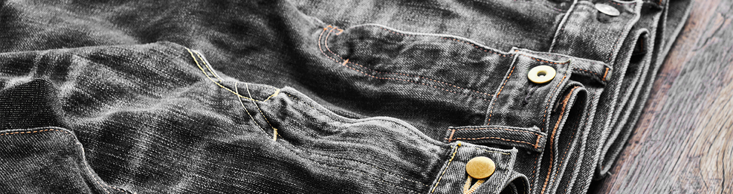 Multiple pairs of washed, clean black jeans folded on a wooden table.