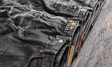 Multiple pairs of washed, clean black jeans folded on a wooden table.